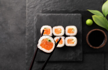 Chopsticks take Sushi roll close up. A set of sushi with salmon and cucumber on black slate boards. Traditional Japanese food. Top view
