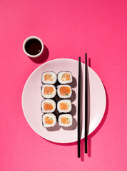 Japanese Sushi roll with salmon, cucumber and soy sauce with chopsticks in the plate on pink...