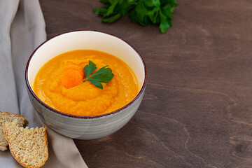 carrot cream soup with fresh carrots and herbs on wooden background. Carrot soup with parsley on brown table. Spring vegetable soup. Homemade cream soup with copy space.