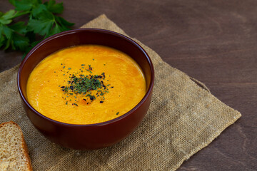 bowl of tasty carrot cream soup with bread and herbs with sackcloth on wooden background.Spring vegetable Homemade Carrot cream soup with parsley on brown table.copy space.