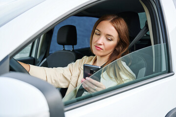Woman is looking on the phone while driving a car. The concept of danger on the road and inattentive car driving - obrazy, fototapety, plakaty