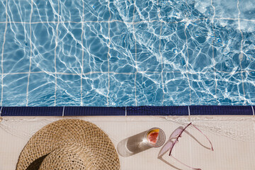 Straw hat, sunglasses and cocktail on swimming pool side. Blue sea surface with waves, texture...