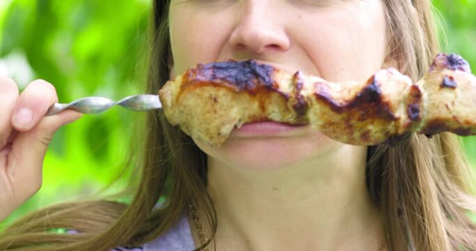 A woman eating a kebab on a skewer, in a Park or forest nature green background