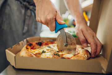 Hand of kitchen chef cutting pizza with a pizza cutter