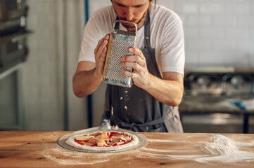 Man worker in a pizza place placing ingredients on pizza dough