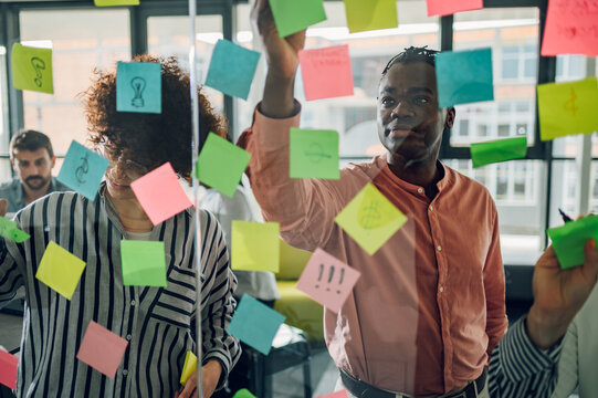 Multiracial Team At Work Writing Ideas On Sticky Notes On The Glass Wall