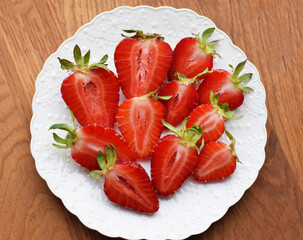 Ripe juicy strawberries cut in halves on a white plate.