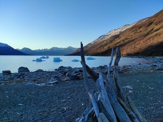 Fototapeta na wymiar Coucher de soleil sur le glacier perrito Moreno, plage et tipi de bois avec iceberg en fond, Patagonie, El Calafate, Argentine