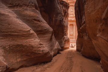 Al Siq Canyon in Petra, Jordan, pink red sandstone walls both sides, unrecognizable person sitting...