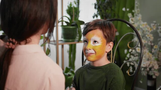 A young woman paints with face painting on the child's face. Children's festival. Face painting, painting with paints on the face of a child