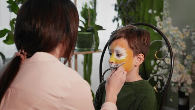 A young woman paints with face painting on the child's face. Children's festival. Face painting, painting with paints on the face of a child