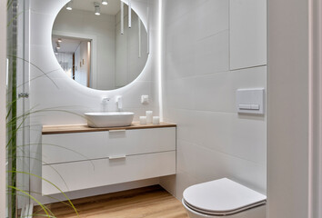 Interior of bathroom with ceramic bowl on the wooden cabinet, wooden tile on the floor, round mirror with led lights. Stylish bathroom with wc and bath. - obrazy, fototapety, plakaty