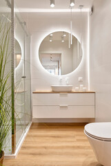Luxury bathroom with glass to shower, round mirror with led lights, stylish washbasin and wooden...