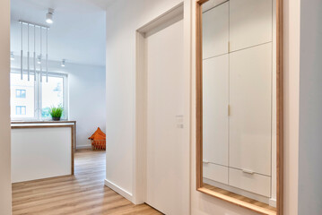 Fototapeta premium Interior of entrance hall in new apartment with wooden floor, big mirror, window and stylish lamp. Corridor with entrance and white door. Room at home.