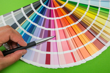 Female hand chooses color in palette swatches. Rainbow colors catalog isolated on green