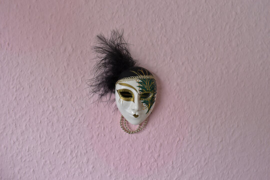 Venetian mask of a harlequin on a pink pastel coloured wall