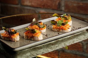 baked bruschetta with salmon, cheese, sun-dried tomatoes and avocado in gray plate on bright background