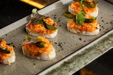 baked bruschetta with salmon, cheese, sun-dried tomatoes and avocado in gray plate on bright background