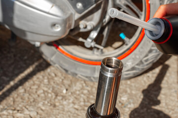 A car mechanic repairs a motorbike. A man pours oil into the shock absorber of the front fork of a scooter