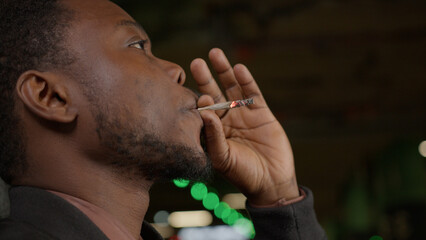 Close-up portrait of an African American smoking medicinal marijuana inhales nicotine doom and exhales. Teenager smokes nicotine cigarette. Harm of smoking, medicinal marijuana.