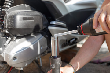 A car mechanic repairs a motorbike. A man pours oil into the shock absorber of the front fork of a...