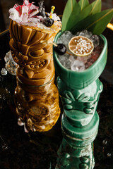 Tiki Drink Cocktails. Two cocktails in different glasses against the background of a bar decorated with dried fruits and tropical leaves.