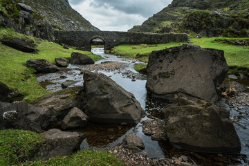 un pont de pierre et une rivière au milieu d'un paysage de montagnes irlandaises