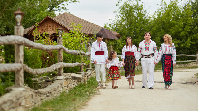 Full length image of a happy family with kids in traditional romanian clothes in a countryside. Father, mother, son and daughters walking outside together.
