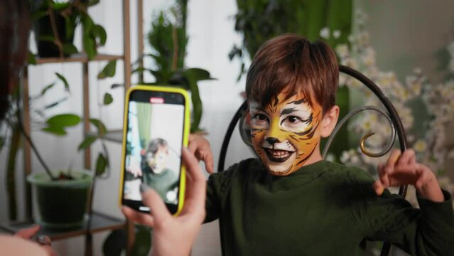 Children's festival. Face painting, painting with paints on the face of a child. Female hands take a picture on the phone of a boy with a painted face