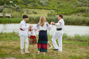 Fototapeta premium Happy family with kids in traditional romanian clothes dancing outside.
