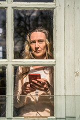 Woman holding smartphone and looking at the window with worried face