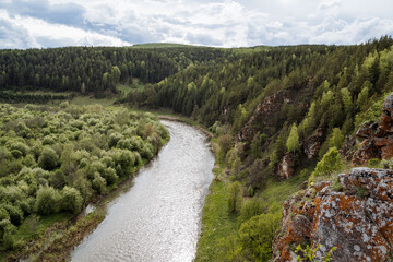 The nature of Russia, the taiga area, the reserved land, the landscape of the mountain river, the orange rock against the background of the green forest, the overcast sky.