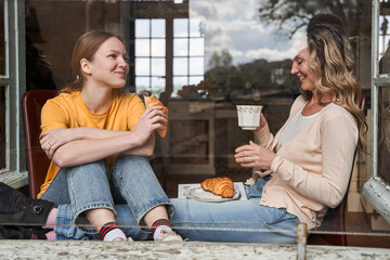 Teen girl spending time with her mother while eating croissants with tea