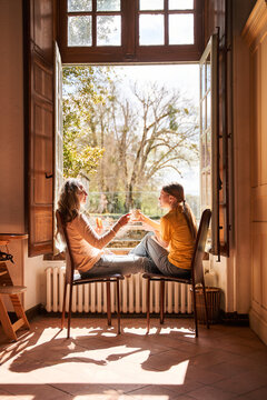 Woman and her daughter enjoying of morning tea together near the window
