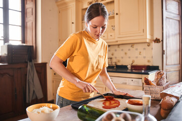 Concentrated teenage girl putting sous with spoon at the pizza while cooking