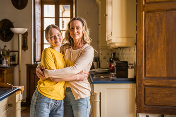 Teen girl embracing her lovely mother while spending time at the kitchen