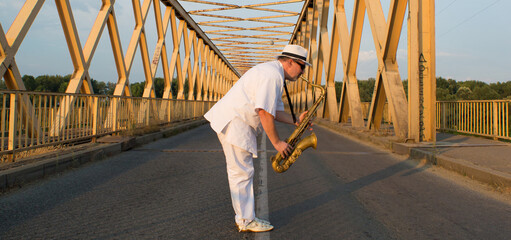 Man playing the saxophone on the bridge while standing in the middle of the road on a sunny summer...