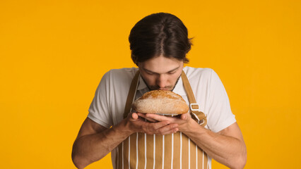 Male baker wearing apron enjoying aroma of bread standing against a colorful background