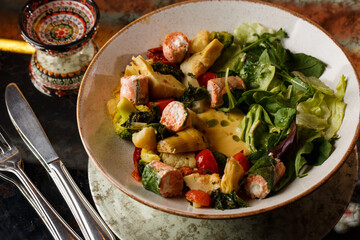 A salad with grilled salmon, mashed avocado and lettuce dressed with cream cheese. Close-up of the dish in a brown bowl isolated on brown background.