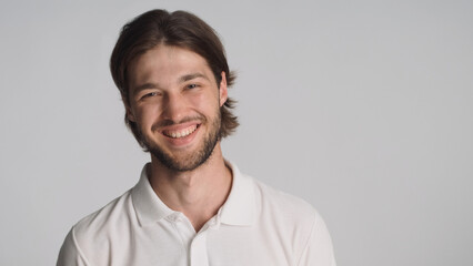 Fototapeta premium Beautiful guy sincerely smiling at camera over gray background. Positive man standing in studio