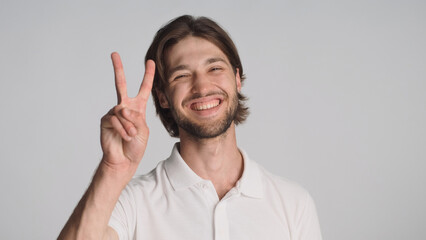 Cheerful guy showing peace sign sincerely smiling at camera over gray background. Young positive...