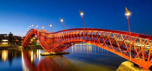 A bridge in the city at night. The bridge against the sky during the blue hour. The Python Bridge, Amsterdam, the Netherlands. Panoramic photography for design and background.. - obrazy, fototapety, plakaty