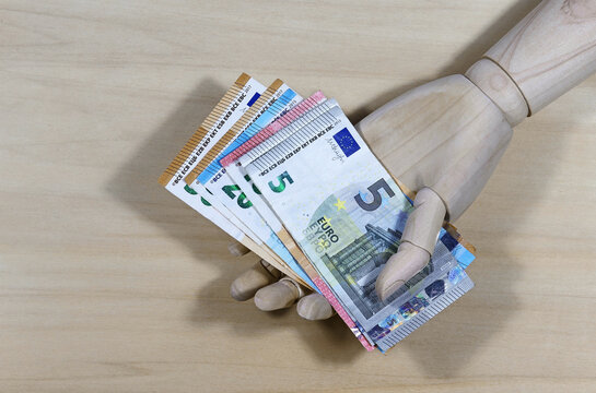 Geld verschenken. Eine Holzhand und Eurogeldscheine