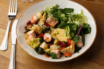 A salad with grilled salmon, mashed avocado and lettuce dressed with cream cheese. Close-up of the dish in a brown bowl isolated on brown background.