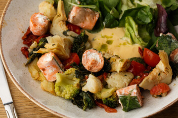 A salad with grilled salmon, mashed avocado and lettuce dressed with cream cheese. Close-up of the dish in a brown bowl isolated on brown background.