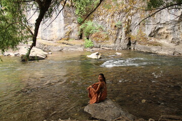 Fototapeta na wymiar Smiling woman sitting on a rock on the river