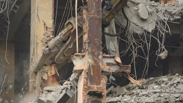 Close up video of a construction excavator destroying the remainings of the building. Camera showing the demolition of the beams inside the building with concrete and trash around.