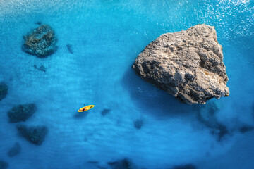 Aerial view of yellow kayak in blue sea at sunset in summer. Man on floating canoe in clear azure water, rocks, stones. Lefkada island, Greece. Tropical landscape. Sup board. Active travel. Top view