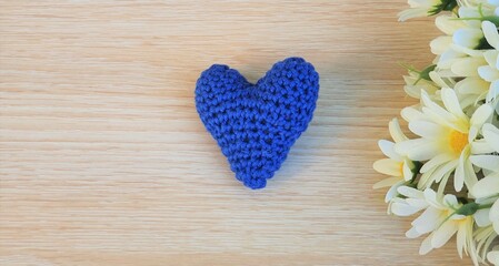 Flowers and a crochet heart on wooden background.