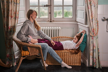 Obraz premium Mother spending time with her daughter, sitting at the sofa and speaking with lovely baby